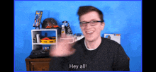 a man wearing glasses says hey all in front of a blue wall