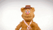 fozzie bear from the muppet show is wearing a hat and tie and waving .