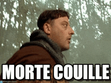 a man with a beard and a sweater is standing in front of a tree with the words morte couille written on it .