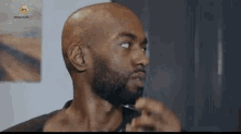 a bald man with a beard is shaving his beard with a razor in front of a mirror .