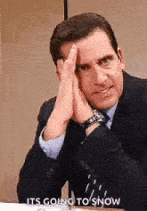 a man in a suit and tie is sitting at a desk with his hands on his forehead .