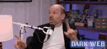 a man sitting in front of a microphone with the words dark web on the bottom right