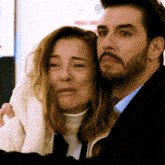 a man with a beard is hugging a woman who is making a sad face