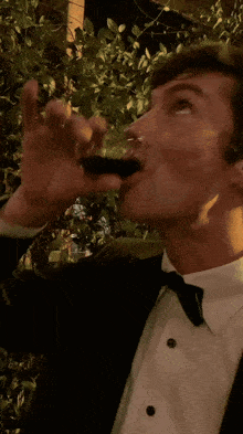 a man in a tuxedo drinks from a shot glass