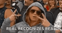 a woman in a hooded jacket and sunglasses is sitting in a crowd of people .