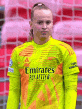 a female soccer player wearing a yellow and orange jersey that says emirates fly better