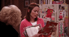 a woman in a pink sweater is reading a book while another woman looks on