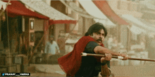 a man in a red cape is holding a stick with the words pranay varma below him