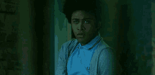 a young man wearing a blue shirt and a grey cardigan is standing in a dark room .