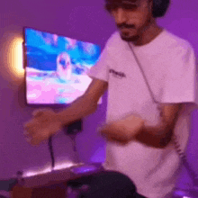 a man wearing headphones is playing a video game in front of a television in a purple room .