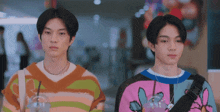two young men wearing colorful sweaters are standing next to each other in a mall