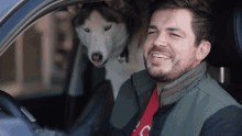 a man is driving a car with a husky dog behind him