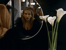 a woman in a black dress is looking at herself in a round mirror