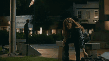 a woman is sitting on a bench in a park at night with a man standing behind her .