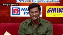 a man in a green shirt is sitting on a red couch in front of a sign that says ' nir pa '
