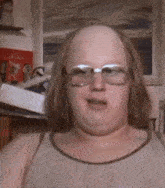 a bald man wearing glasses and a tank top looks at the camera .