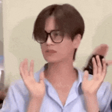 a man wearing glasses and a blue shirt is making a funny face with his hands .