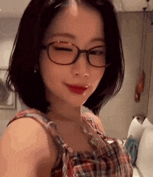 a young woman wearing glasses and a plaid shirt is looking at the camera .