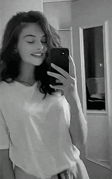 a woman is taking a selfie with her phone in front of a mirror .