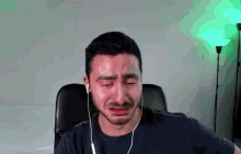 a man wearing headphones is crying while sitting in a chair in front of a green lamp .