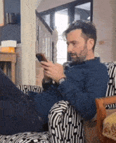 a man in a blue shirt is laying on a chair looking at his phone