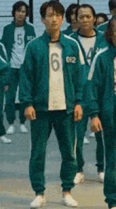 a man in a green uniform with the number 6 on his shirt is standing in a line with other people .
