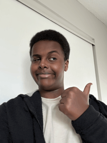 a young man in a black jacket is giving a thumbs up sign