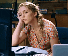 a woman is sitting at a desk with her hand on her face