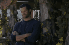 a man in a blue sweater leans against a tree
