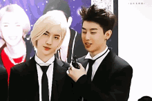 two men in suits and ties are standing next to each other and one is holding a cell phone