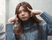 a woman in a blue sweater is making a funny face with her hands .