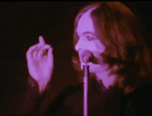 a woman singing into a microphone with a purple light behind her