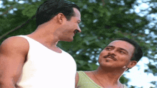 a man with a mustache looks at another man in a white tank top