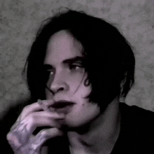 a black and white photo of a man with a tattoo on his hand smoking a cigarette .