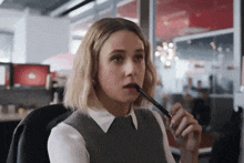 a woman is holding a pen to her mouth while sitting at a desk .