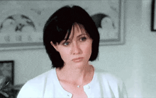 a woman with short black hair is wearing a white cardigan and necklace .