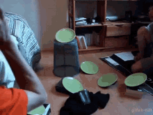 a group of people are playing a game with green plates and glasses on the floor .