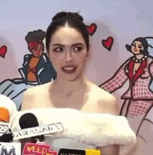 a woman without a shirt is standing in front of a microphone in front of a cartoon wall .