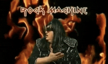 a woman wearing sunglasses is standing in front of a fire with the words rock machine written in white letters .