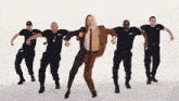 a man in a suit and tie is dancing with a group of men in black uniforms