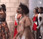 a group of women in dresses are standing next to each other in front of a brick wall .