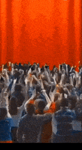 a crowd of people with their arms in the air in front of a red curtain