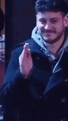 a man with a beard is standing in a dark room with his hands folded in prayer .
