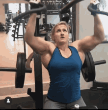 a woman in a blue tank top is lifting a barbell in a gym with the time of 0 13