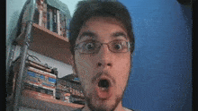 a man with glasses is making a surprised face in front of a bookshelf
