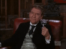 a man in a suit is sitting in a chair holding a glass of wine in front of a fox classics logo
