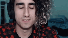 a young man with curly hair is wearing headphones and looking down .