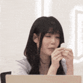 a woman sitting in front of a laptop holding a white object in her hands