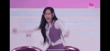a woman in a purple vest and white shirt is dancing on a pink stage .