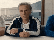 a man in a blue and white jacket is sitting at a table with other people .